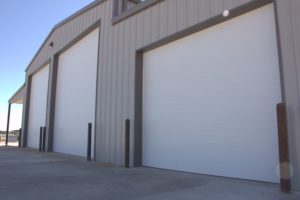 Gray commercial building with three white overhead doors in various sizes
