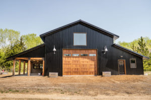 Dark gray carriage house with natural wood overhead door containing four window panels