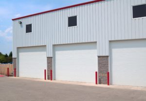 Light gray metal commercial building with three white overhead doors and windows above them